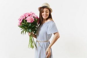Jeune femme tendre en robe bleue, chapeau tenant un bouquet de belles fleurs de pivoines roses isolées sur fond blanc. Concept de fête de la Saint-Valentin, de la Journée internationale de la femme. Espace publicitaire