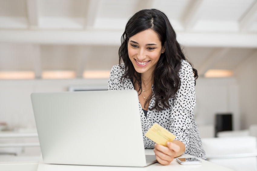 Jeune femme heureuse tenant une carte de crédit et faisant des achats en ligne à la maison. Belle fille utilisant un ordinateur portable pour faire des achats en ligne avec une carte de crédit. Femme souriante utilisant un ordinateur portable et une carte de crédit pour un paiement en ligne.