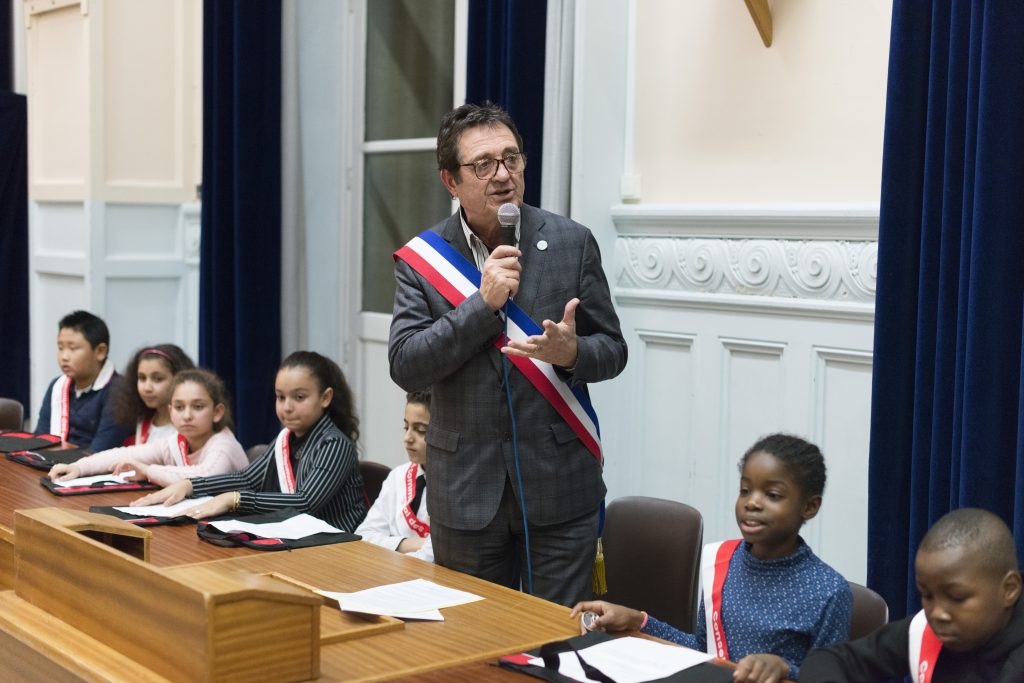 le maire entouré d'enfants élus parle au micro