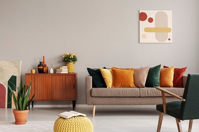Peinture abstraite sur le mur gris d'un intérieur de salon rétro avec canapé beige avec coussins, fauteuil vintage vert foncé et pouf jaune avec livre